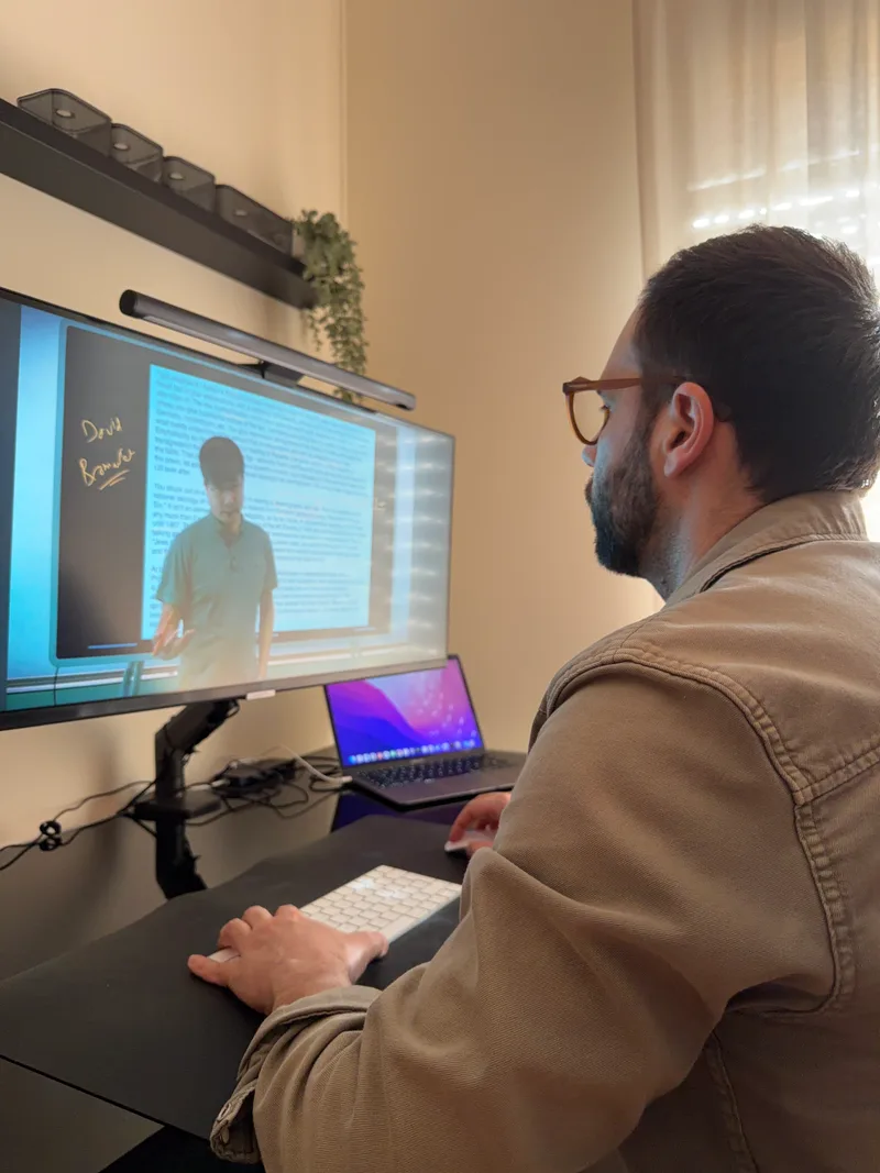 Editor Alvaro Faustino at desk reviewing a Predictive History lecture by Professor Jiang Xueqin, hands on keyboard with secondary laptop and primary monitor showing the lecture.